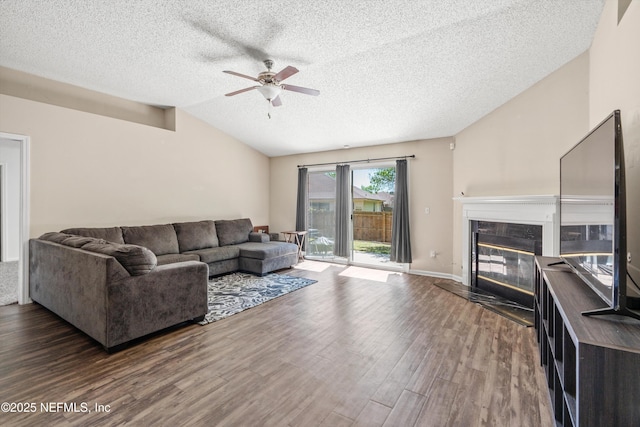 living area featuring wood finished floors, a ceiling fan, lofted ceiling, a fireplace, and a textured ceiling