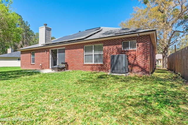 back of house with a yard, brick siding, solar panels, and fence