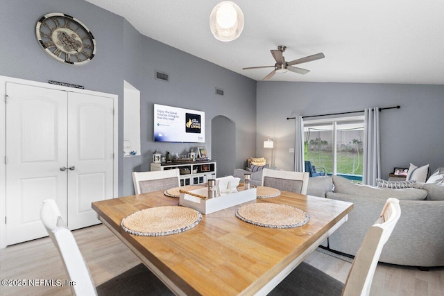 dining space featuring light wood-type flooring, visible vents, arched walkways, lofted ceiling, and ceiling fan