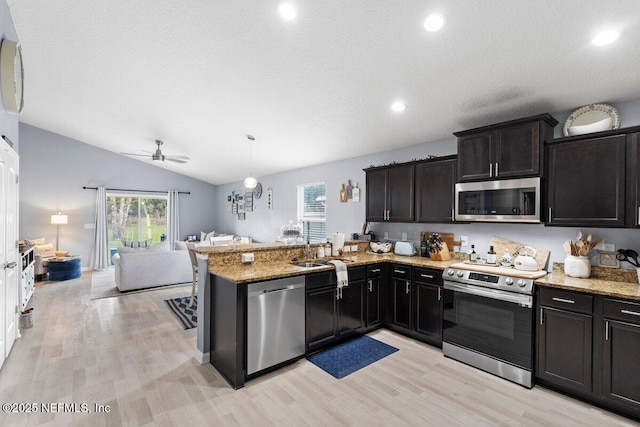 kitchen featuring light stone countertops, open floor plan, vaulted ceiling, appliances with stainless steel finishes, and a peninsula