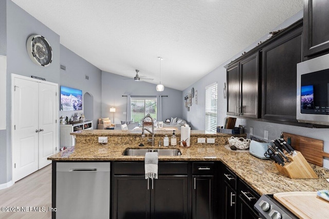 kitchen with a sink, light stone counters, appliances with stainless steel finishes, a peninsula, and lofted ceiling