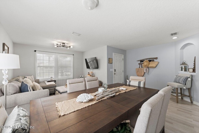 dining area featuring visible vents, baseboards, light wood-type flooring, arched walkways, and a textured ceiling