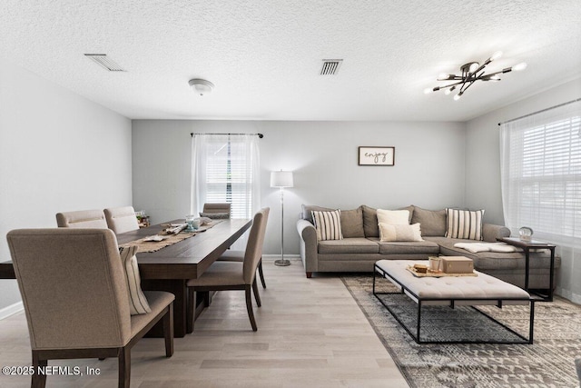 living area featuring visible vents, a textured ceiling, a chandelier, and light wood finished floors