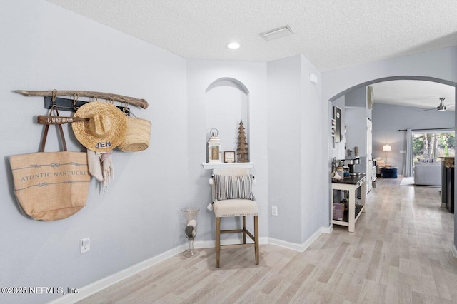 hall featuring wood finished floors, arched walkways, and a textured ceiling