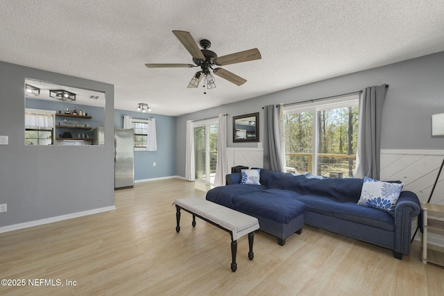 living area with a textured ceiling, wainscoting, light wood-type flooring, and ceiling fan