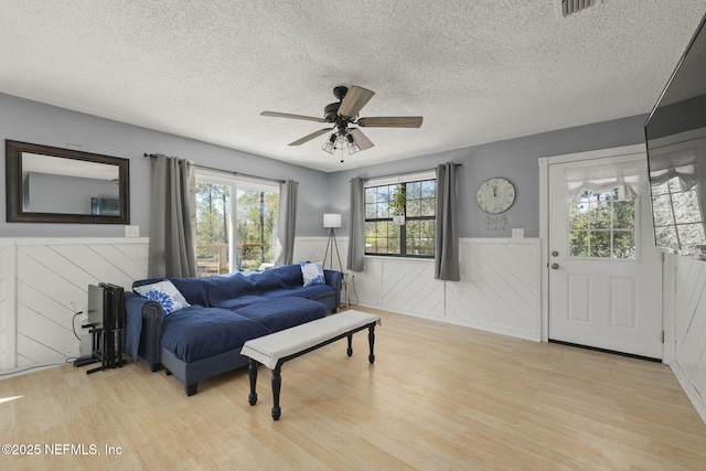 living room with a wainscoted wall, a textured ceiling, ceiling fan, and wood finished floors