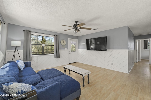 living area featuring ceiling fan, a wainscoted wall, and wood finished floors