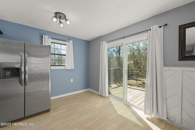 unfurnished dining area with baseboards, a textured ceiling, and light wood finished floors