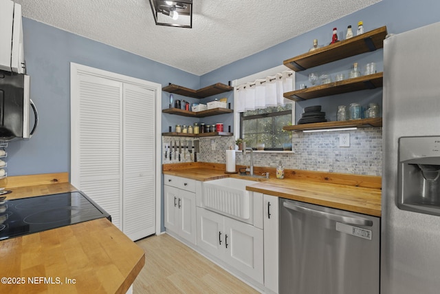 kitchen featuring open shelves, stainless steel appliances, butcher block countertops, and a sink