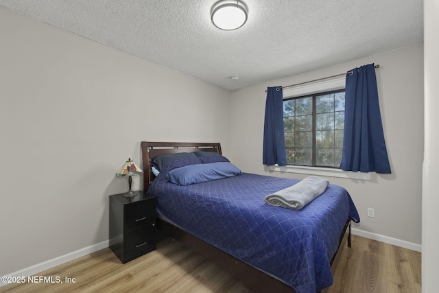 bedroom featuring a textured ceiling, baseboards, and wood finished floors