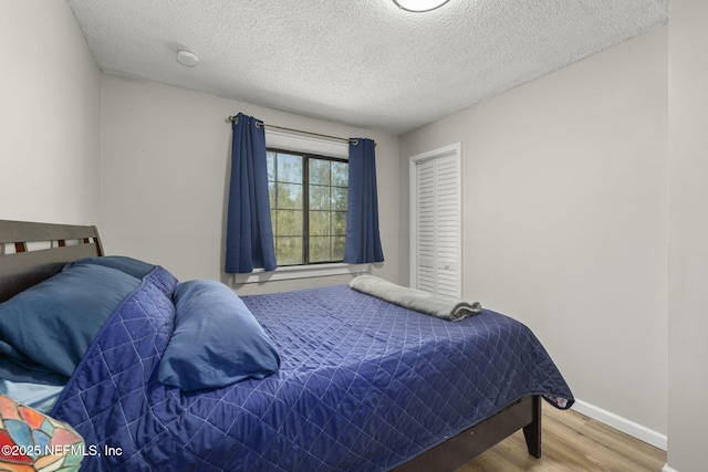 bedroom featuring baseboards, a textured ceiling, and wood finished floors