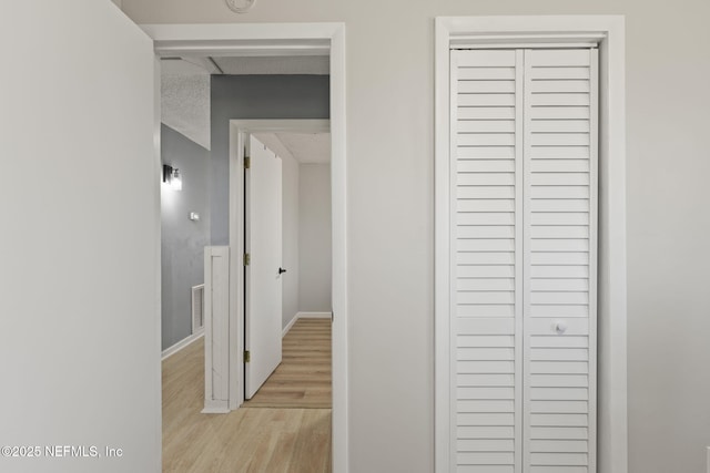 hallway featuring visible vents, light wood-style flooring, a textured ceiling, and baseboards