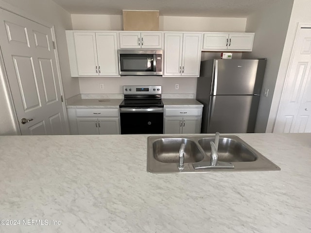 kitchen featuring white cabinets, stainless steel appliances, light countertops, and a sink