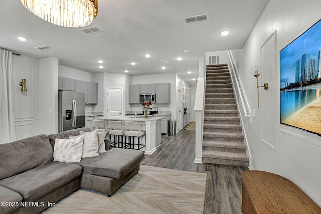 living room featuring stairs, dark wood-style floors, and visible vents