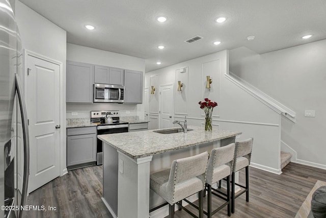 kitchen with light stone countertops, visible vents, dark wood-style flooring, gray cabinetry, and appliances with stainless steel finishes