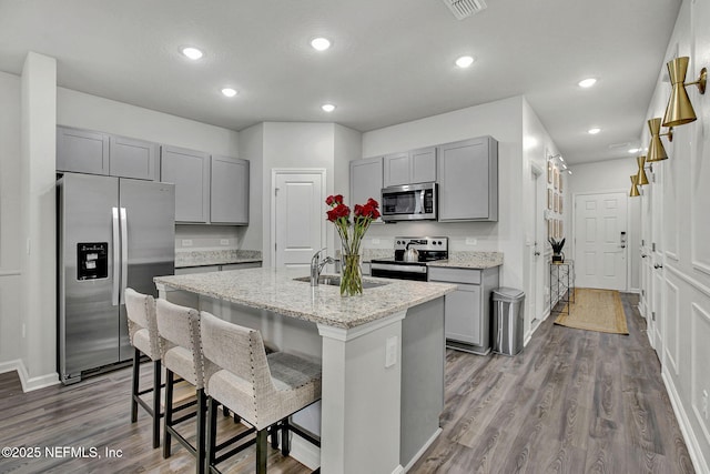 kitchen featuring a kitchen bar, gray cabinetry, a sink, light stone counters, and appliances with stainless steel finishes