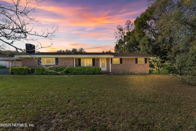 single story home featuring a carport, cooling unit, brick siding, and a front yard