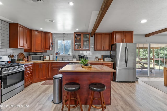 kitchen featuring a breakfast bar area, light wood finished floors, a sink, appliances with stainless steel finishes, and beamed ceiling