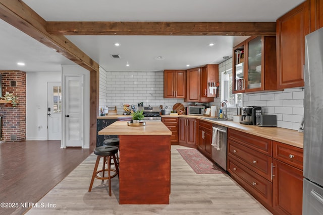 kitchen with a kitchen bar, beamed ceiling, butcher block countertops, stainless steel appliances, and light wood finished floors