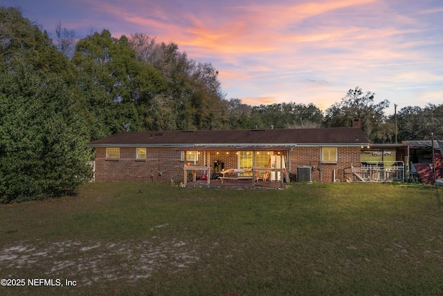 back of house featuring brick siding, central AC, a chimney, a patio area, and a lawn