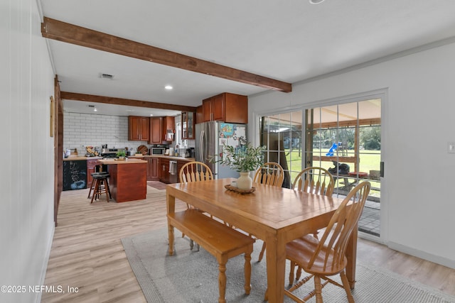 dining room with light wood-type flooring, beamed ceiling, baseboards, and visible vents