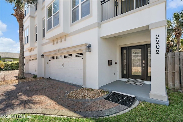 doorway to property with decorative driveway, a garage, and stucco siding