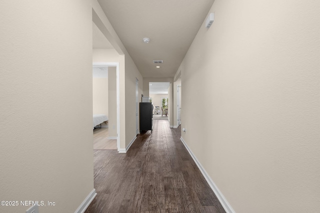 corridor with visible vents, baseboards, and dark wood-style floors