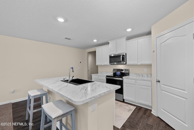 kitchen featuring visible vents, range with electric cooktop, an island with sink, a sink, and stainless steel microwave