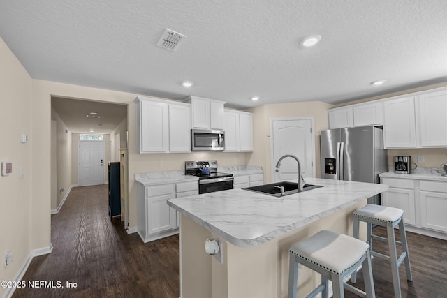 kitchen featuring visible vents, dark wood finished floors, a kitchen island with sink, a sink, and stainless steel appliances