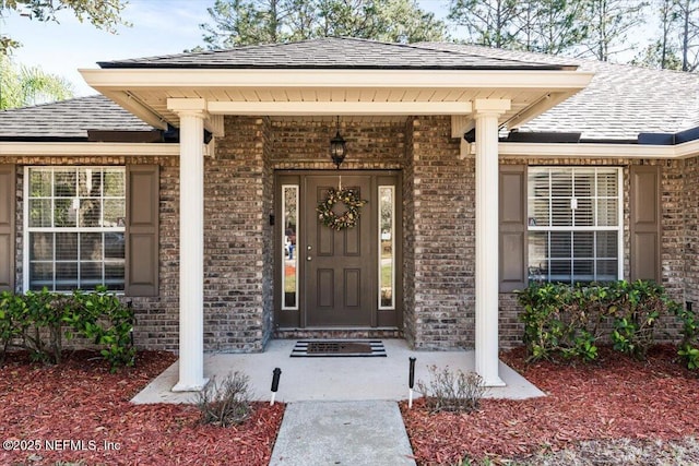 doorway to property featuring brick siding and a shingled roof