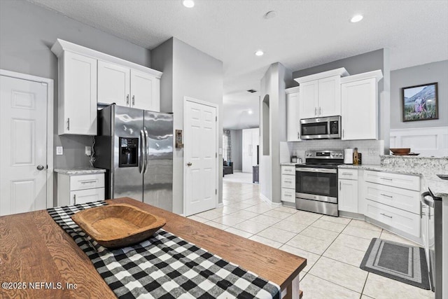 kitchen featuring tasteful backsplash, light tile patterned floors, light stone counters, appliances with stainless steel finishes, and white cabinets