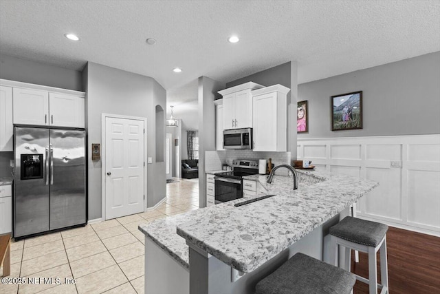 kitchen with white cabinetry, a sink, light stone countertops, and stainless steel appliances