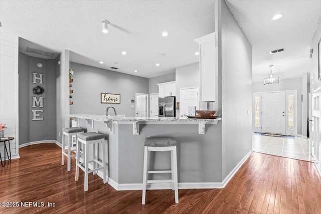 kitchen with a breakfast bar area, light stone counters, hardwood / wood-style flooring, white cabinets, and stainless steel fridge