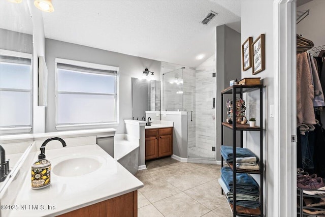 bathroom featuring visible vents, two vanities, a sink, a shower stall, and a textured ceiling