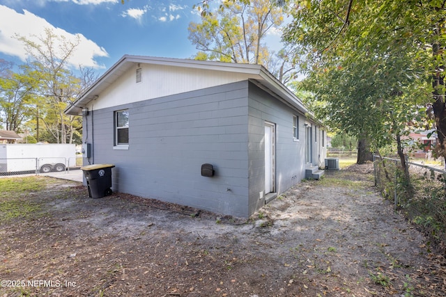 view of side of property featuring concrete block siding, central AC unit, and fence