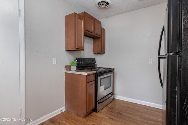 kitchen featuring visible vents, light wood-type flooring, brown cabinets, freestanding refrigerator, and electric stove