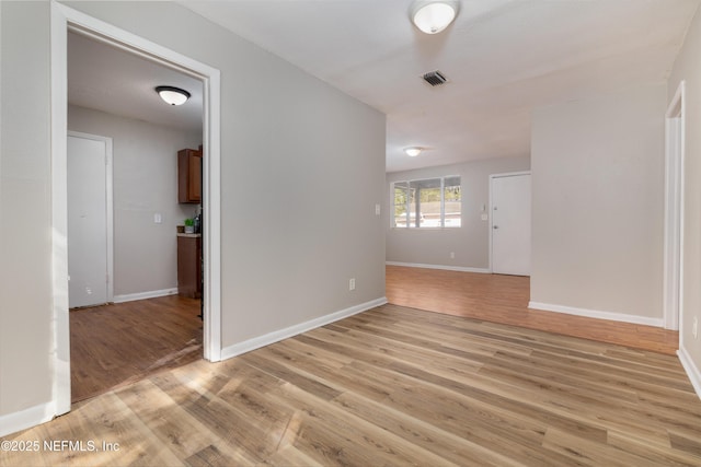 empty room featuring visible vents, light wood-type flooring, and baseboards