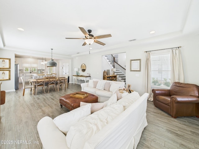 living area with stairs, visible vents, light wood finished floors, and ceiling fan