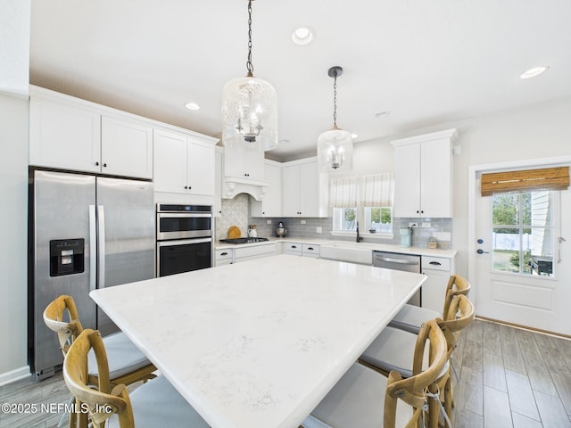 kitchen with backsplash, decorative light fixtures, a breakfast bar, appliances with stainless steel finishes, and white cabinets