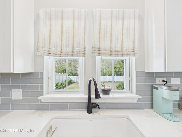 interior details featuring tasteful backsplash, white cabinets, light stone countertops, and a sink