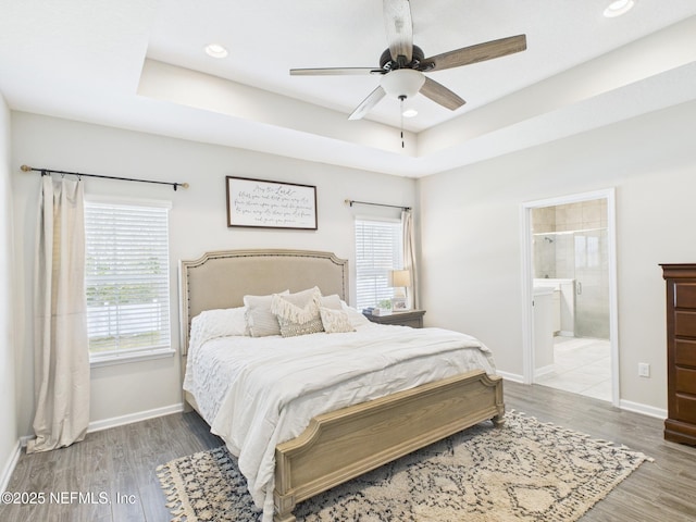bedroom featuring recessed lighting, a tray ceiling, baseboards, and wood finished floors