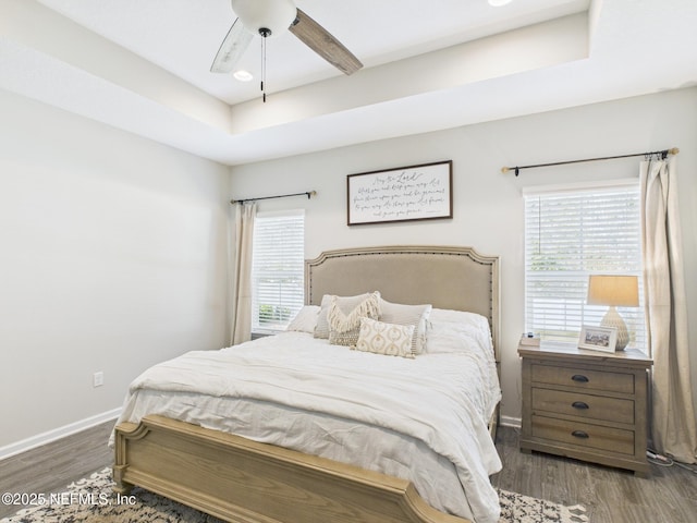 bedroom with a ceiling fan, a tray ceiling, wood finished floors, and baseboards