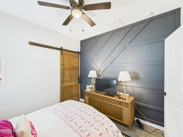bedroom with a barn door, wood finished floors, a ceiling fan, and a decorative wall