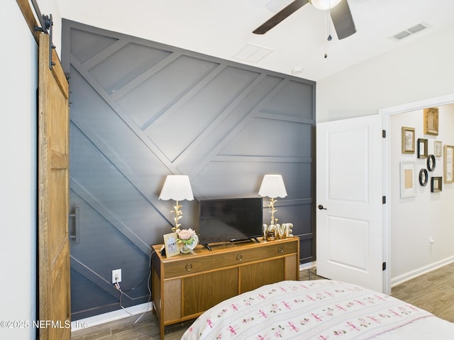 bedroom with a barn door, a decorative wall, wood finished floors, and visible vents
