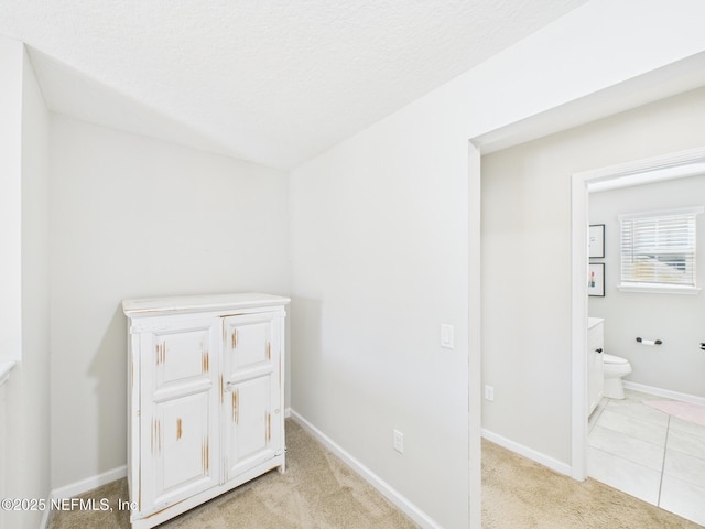 interior space with connected bathroom, baseboards, light colored carpet, and a textured ceiling