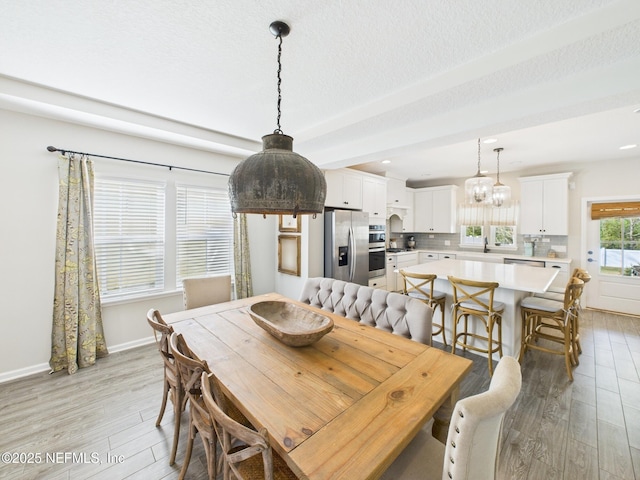 dining space with baseboards, light wood-style floors, a chandelier, and a textured ceiling