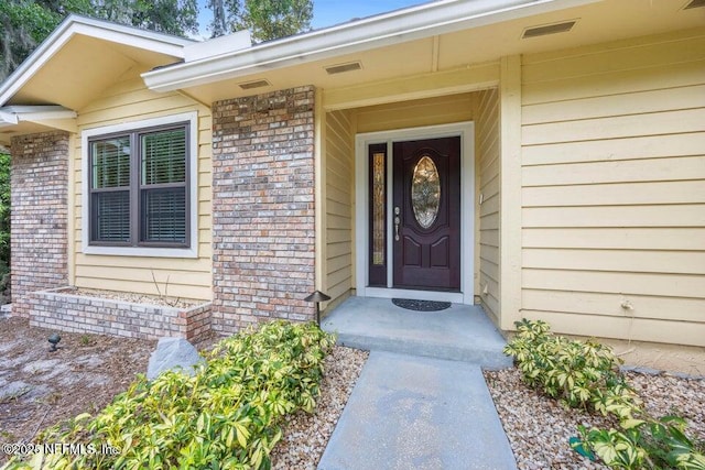 view of exterior entry featuring visible vents and brick siding