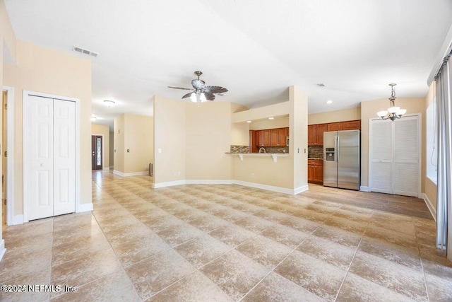 unfurnished living room featuring ceiling fan with notable chandelier, visible vents, and baseboards