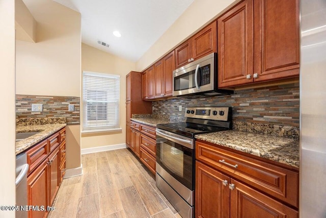 kitchen with visible vents, light wood-style flooring, stone countertops, vaulted ceiling, and appliances with stainless steel finishes