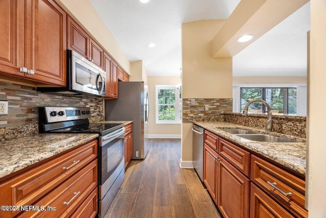 kitchen featuring dark wood-type flooring, baseboards, light stone countertops, appliances with stainless steel finishes, and a sink